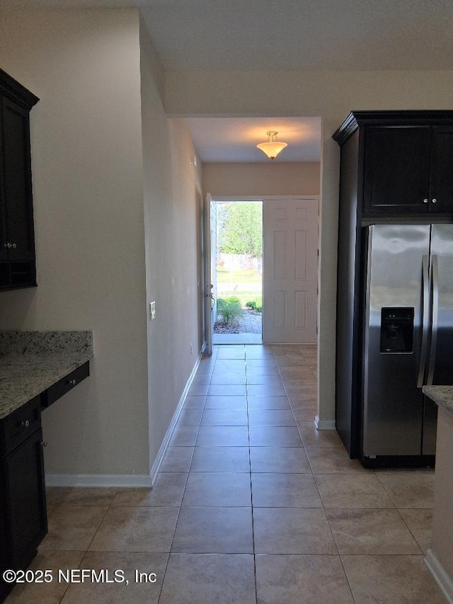kitchen with baseboards, light stone counters, stainless steel fridge, and light tile patterned floors