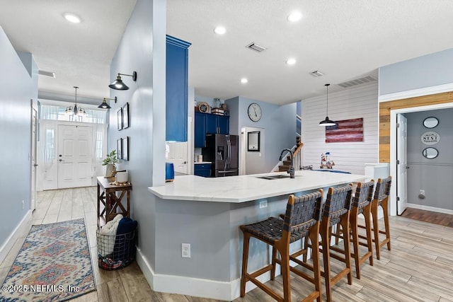 45103 Amhurst Oaks Dr, Callahan, FL 32011 - kitchen with stainless steel refrigerator with ice dispenser, blue cabinetry, a sink, a peninsula, and light wood-type flooring