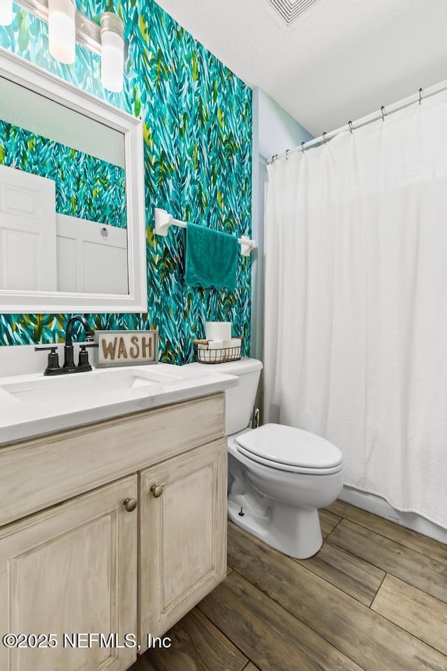 45103 Amhurst Oaks Dr, Callahan, FL 32011 - bathroom with wallpapered walls, wood finished floors, toilet, vanity, and a shower with shower curtain