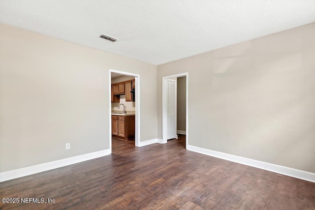 spare room featuring dark wood-style flooring, baseboards, visible vents, and a sink