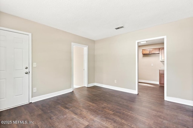 empty room featuring visible vents, dark wood-style flooring, and baseboards