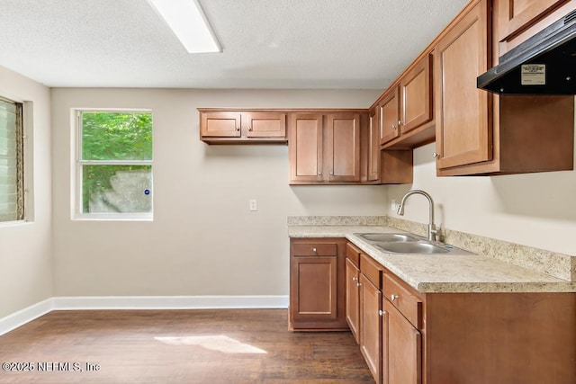 kitchen with a sink, light countertops, dark wood finished floors, baseboards, and under cabinet range hood