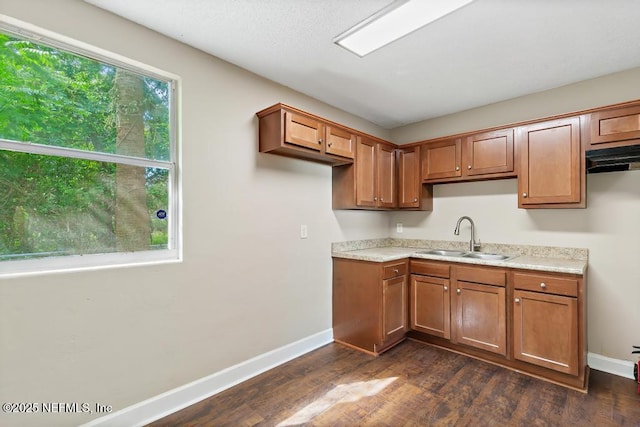 kitchen featuring brown cabinetry, dark wood-style flooring, baseboards, light countertops, and a sink