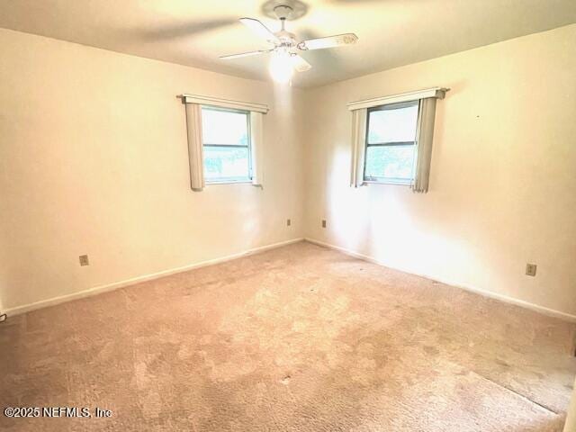 carpeted spare room with healthy amount of natural light, a ceiling fan, and baseboards