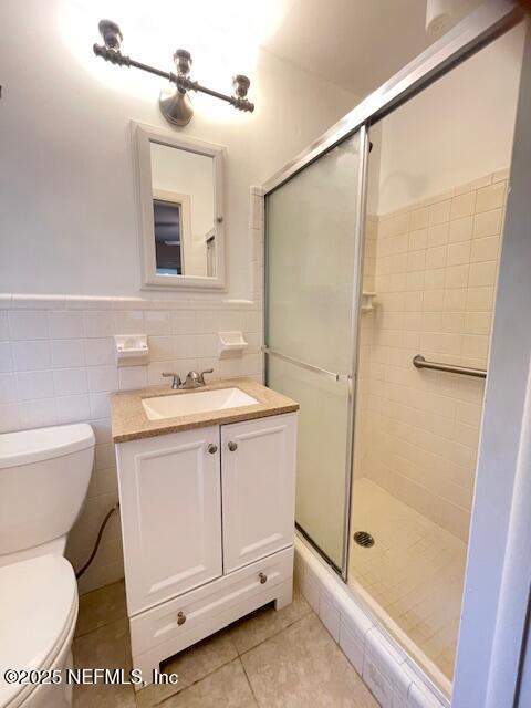 bathroom featuring a stall shower, tile patterned flooring, toilet, vanity, and tile walls