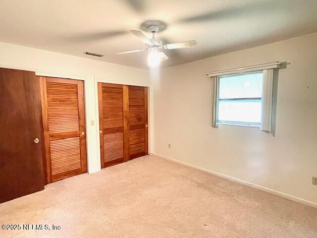 unfurnished bedroom with two closets, carpet, baseboards, and ceiling fan