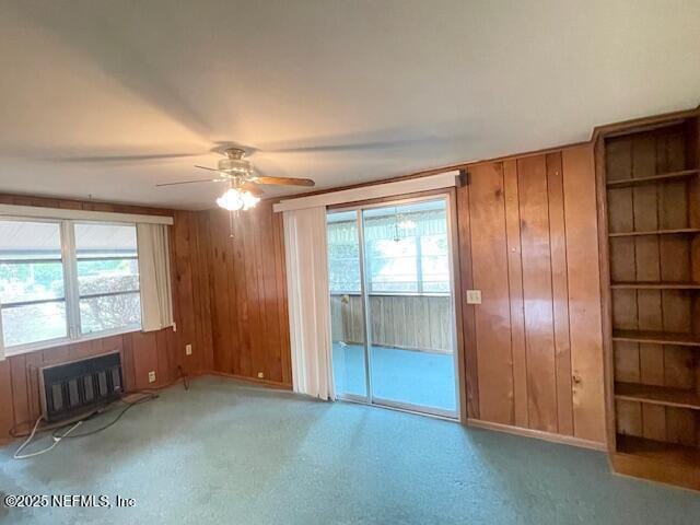 empty room featuring wood walls, healthy amount of natural light, ceiling fan, a fireplace, and baseboards