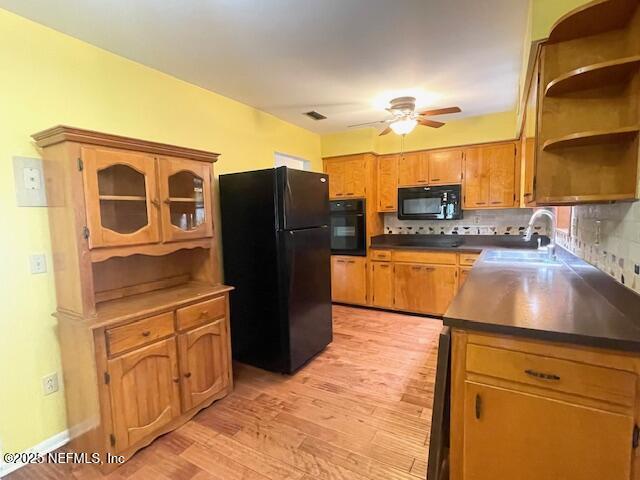 kitchen featuring black appliances, a sink, ceiling fan, light wood-style flooring, and dark countertops