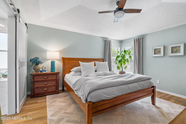 1421 Kipling Ln, Ponte Vedra, FL 32081 - bedroom featuring a barn door, a textured ceiling, light wood finished floors, baseboards, and a ceiling fan