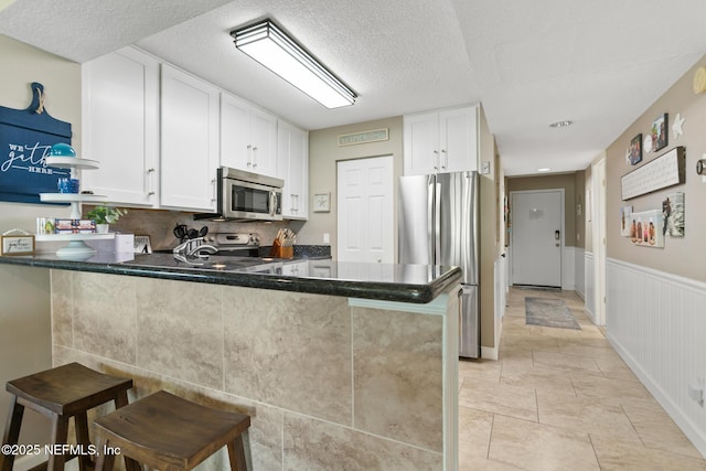 kitchen featuring a peninsula, white cabinetry, appliances with stainless steel finishes, and a breakfast bar area