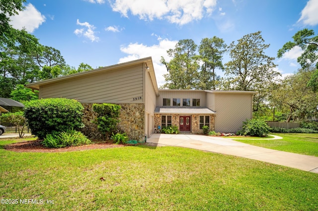 mid-century inspired home with a front lawn, fence, driveway, and stone siding