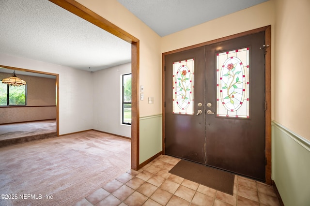entryway with light carpet, baseboards, a textured ceiling, french doors, and light tile patterned floors
