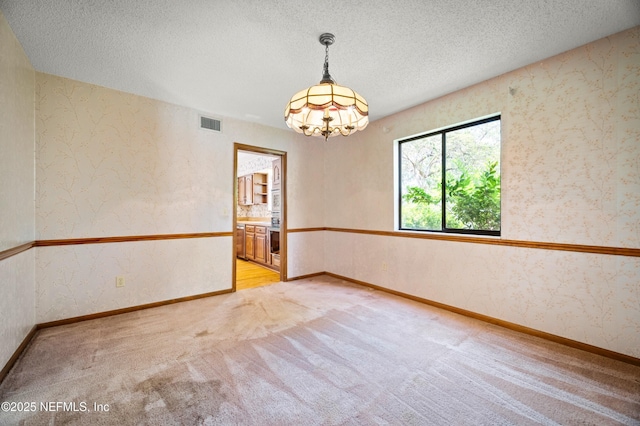 empty room with an inviting chandelier, light colored carpet, a textured ceiling, and visible vents