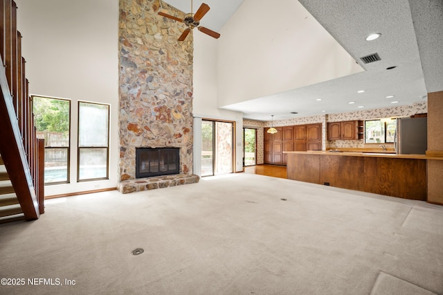 unfurnished living room with a ceiling fan, a stone fireplace, light colored carpet, visible vents, and high vaulted ceiling