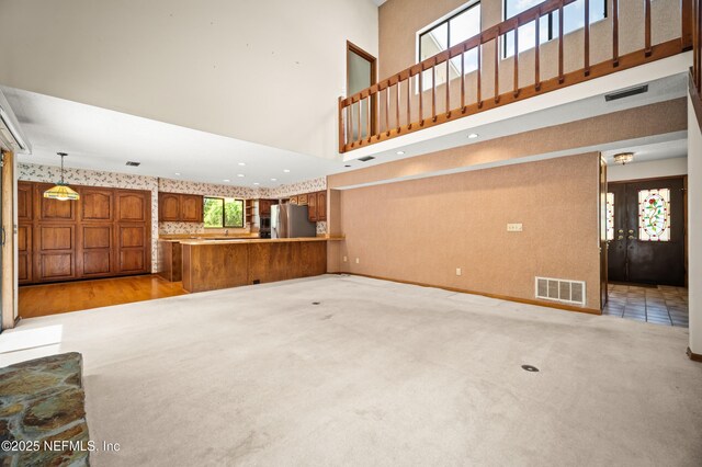 unfurnished living room with visible vents, a towering ceiling, and light carpet