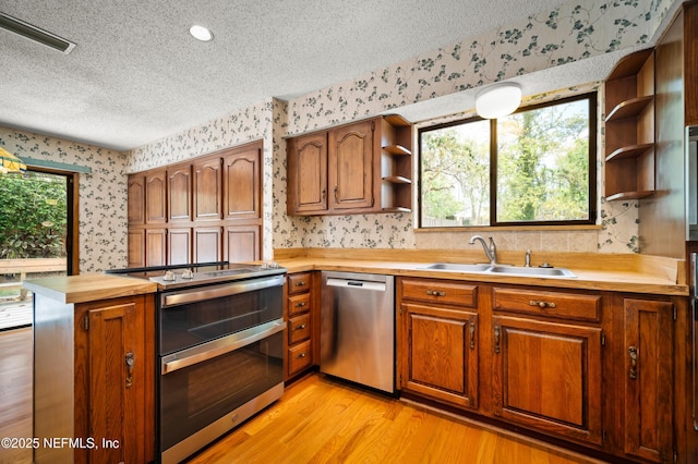 kitchen with open shelves, wallpapered walls, a textured ceiling, a sink, and appliances with stainless steel finishes