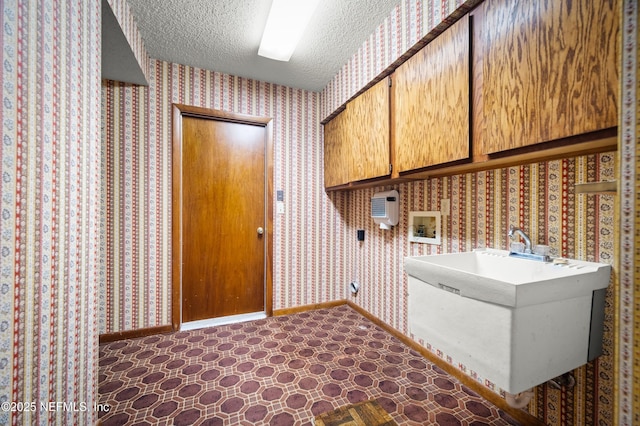 clothes washing area with hookup for a washing machine, cabinet space, a textured ceiling, and wallpapered walls