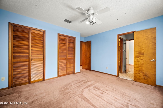 unfurnished bedroom with a textured ceiling, visible vents, carpet floors, baseboards, and two closets