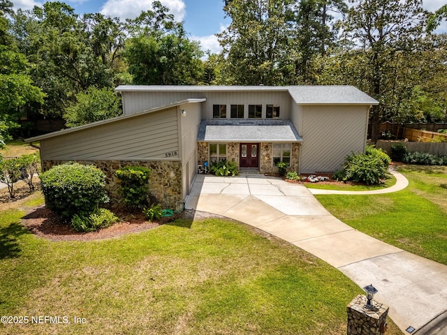 mid-century home featuring fence, driveway, stone siding, and a front yard