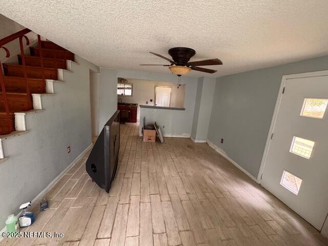 unfurnished living room featuring light wood-style floors, ceiling fan, stairs, and a textured ceiling