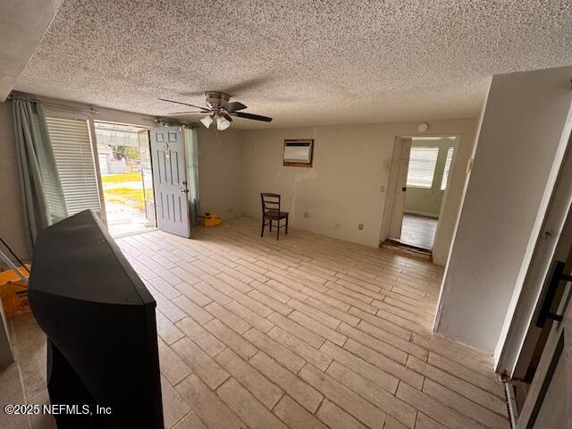 unfurnished living room featuring a textured ceiling, ceiling fan, a wall mounted AC, and plenty of natural light