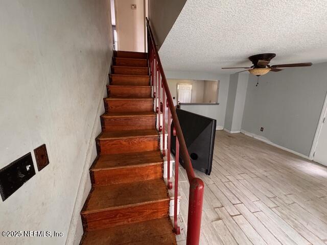 stairway with a ceiling fan, a textured ceiling, and wood finished floors
