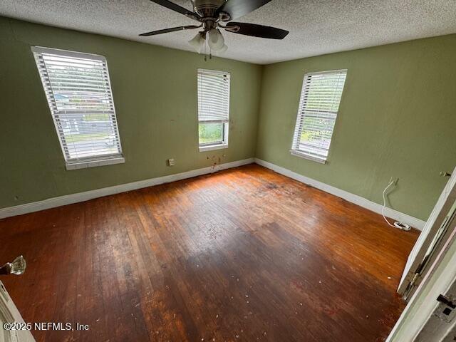unfurnished room featuring baseboards, ceiling fan, a textured ceiling, and wood finished floors