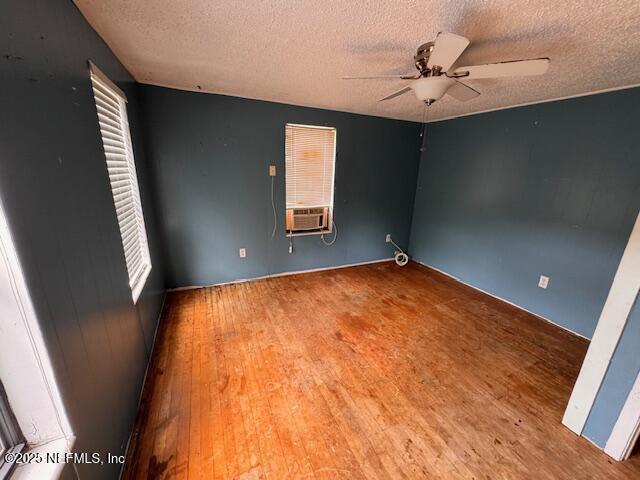 empty room featuring ceiling fan, cooling unit, a textured ceiling, and wood finished floors