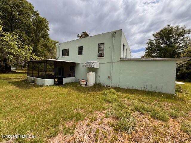 back of house featuring a sunroom, stucco siding, and a yard