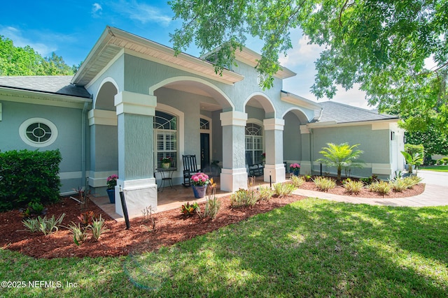 view of front of house featuring a shingled roof, covered porch, stucco siding, and a front yard