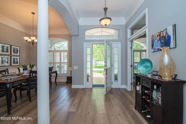 entryway featuring baseboards, ornamental molding, wood finished floors, and a notable chandelier