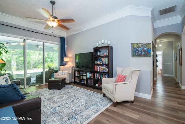 living room with visible vents, ornamental molding, wood finished floors, ceiling fan, and arched walkways