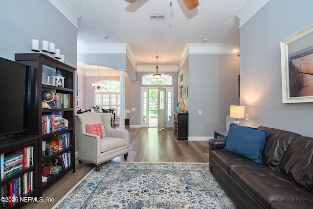 living room with ornate columns, visible vents, wood finished floors, and ceiling fan with notable chandelier