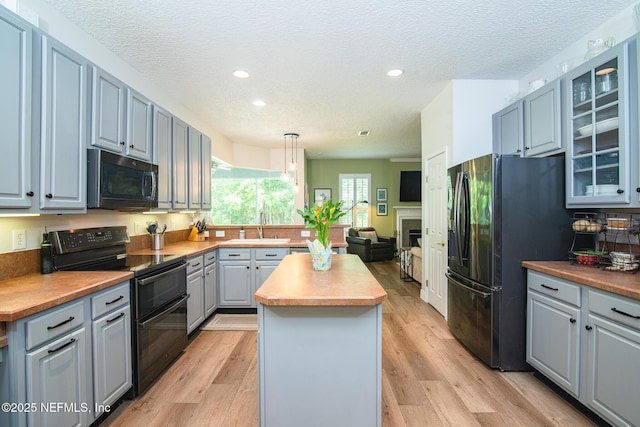 kitchen with a kitchen island, glass insert cabinets, gray cabinets, a sink, and black appliances
