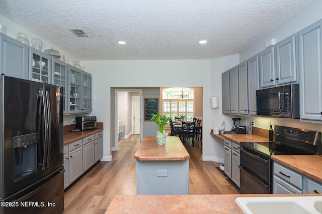 kitchen featuring visible vents, a center island, light wood-style flooring, black appliances, and gray cabinetry