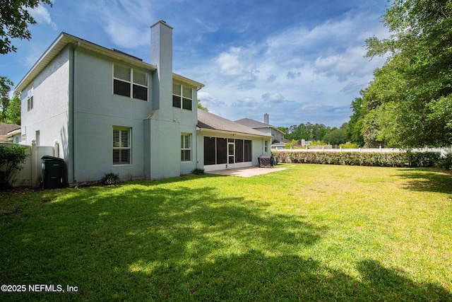 back of house featuring fence, stucco siding, a chimney, a sunroom, and a lawn
