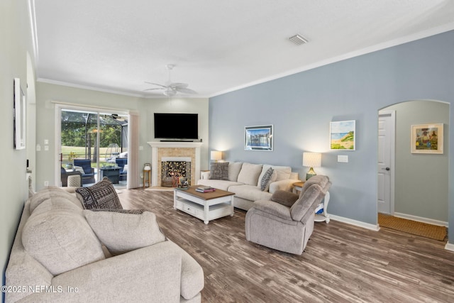living area featuring crown molding, arched walkways, a ceiling fan, baseboards, and wood finished floors