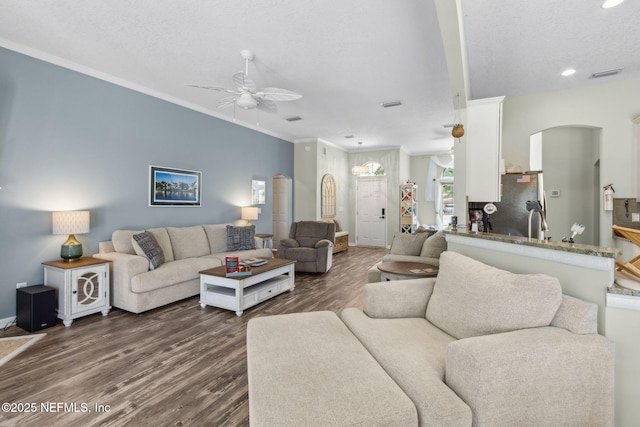 living area featuring arched walkways, ornamental molding, a ceiling fan, recessed lighting, and dark wood-style floors
