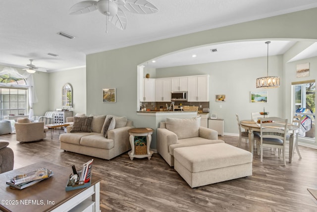 living area with arched walkways, visible vents, dark wood-style floors, and ceiling fan with notable chandelier