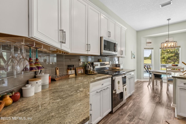 kitchen with white cabinets, appliances with stainless steel finishes, wood finished floors, backsplash, and visible vents