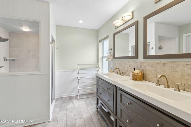 full bath featuring a sink, double vanity, and tiled shower