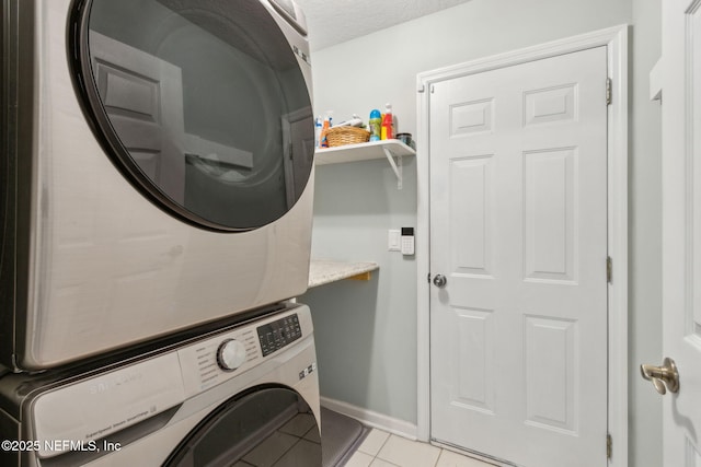 laundry room featuring laundry area, baseboards, light tile patterned flooring, and stacked washer / dryer