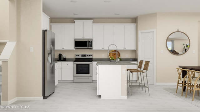 kitchen featuring white cabinets, appliances with stainless steel finishes, a breakfast bar, and light wood-type flooring