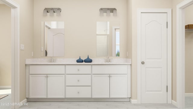 bathroom with double vanity, baseboards, a closet, and a sink