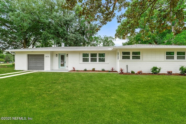 ranch-style home featuring concrete block siding, roof with shingles, a front yard, and a garage