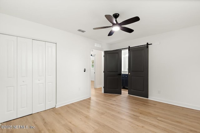 unfurnished bedroom with visible vents, light wood-type flooring, a barn door, baseboards, and a closet