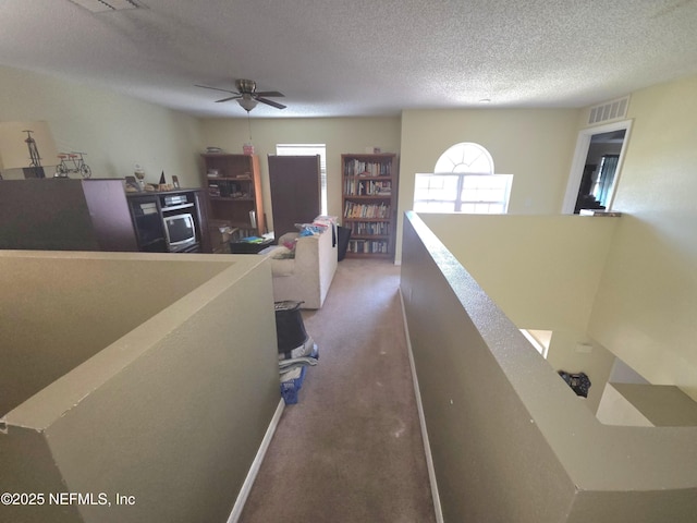hallway with visible vents, carpet flooring, a textured ceiling, and an upstairs landing