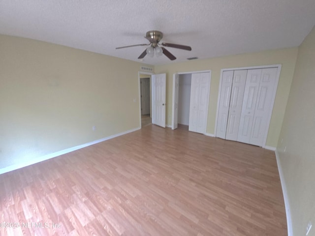 unfurnished bedroom with baseboards, a ceiling fan, two closets, and light wood-type flooring