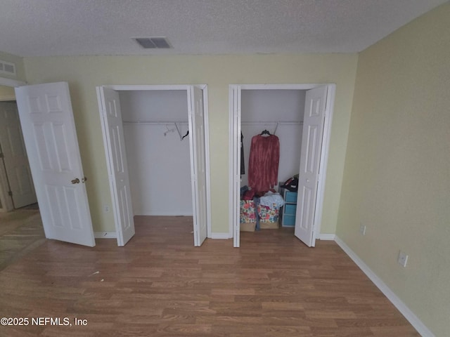 unfurnished bedroom with a textured ceiling, two closets, baseboards, wood finished floors, and visible vents