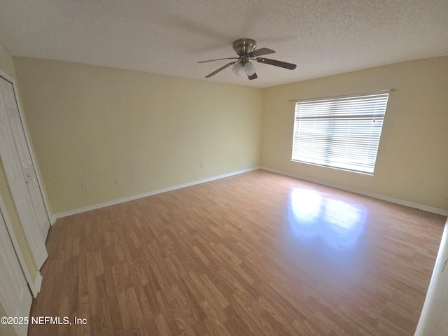 unfurnished room featuring baseboards, a ceiling fan, a textured ceiling, and wood finished floors